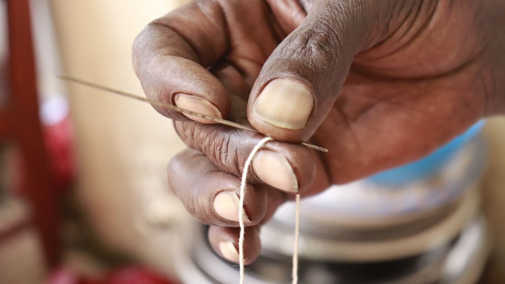 main sugu Gros plan de la main d’une femme enfilant une aiguille avec du fil de coton, mettant en valeur la précision et le savoir-faire en matière de couture ou de couture
